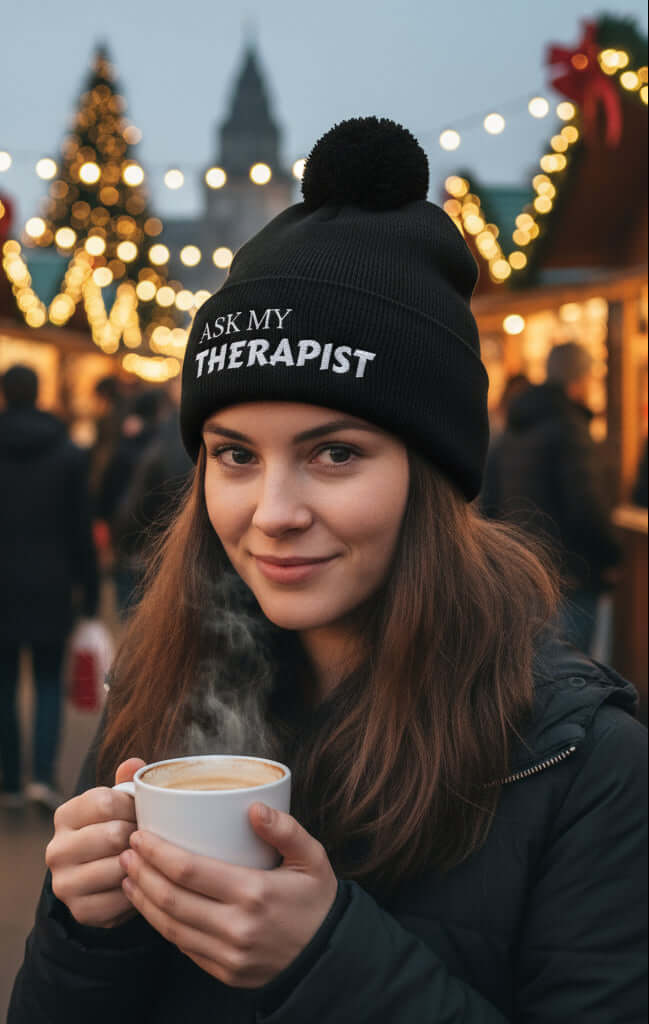 Woman wearing Ask My Therapist Embroidered Bobble Hat while sipping coffee at a festive market.