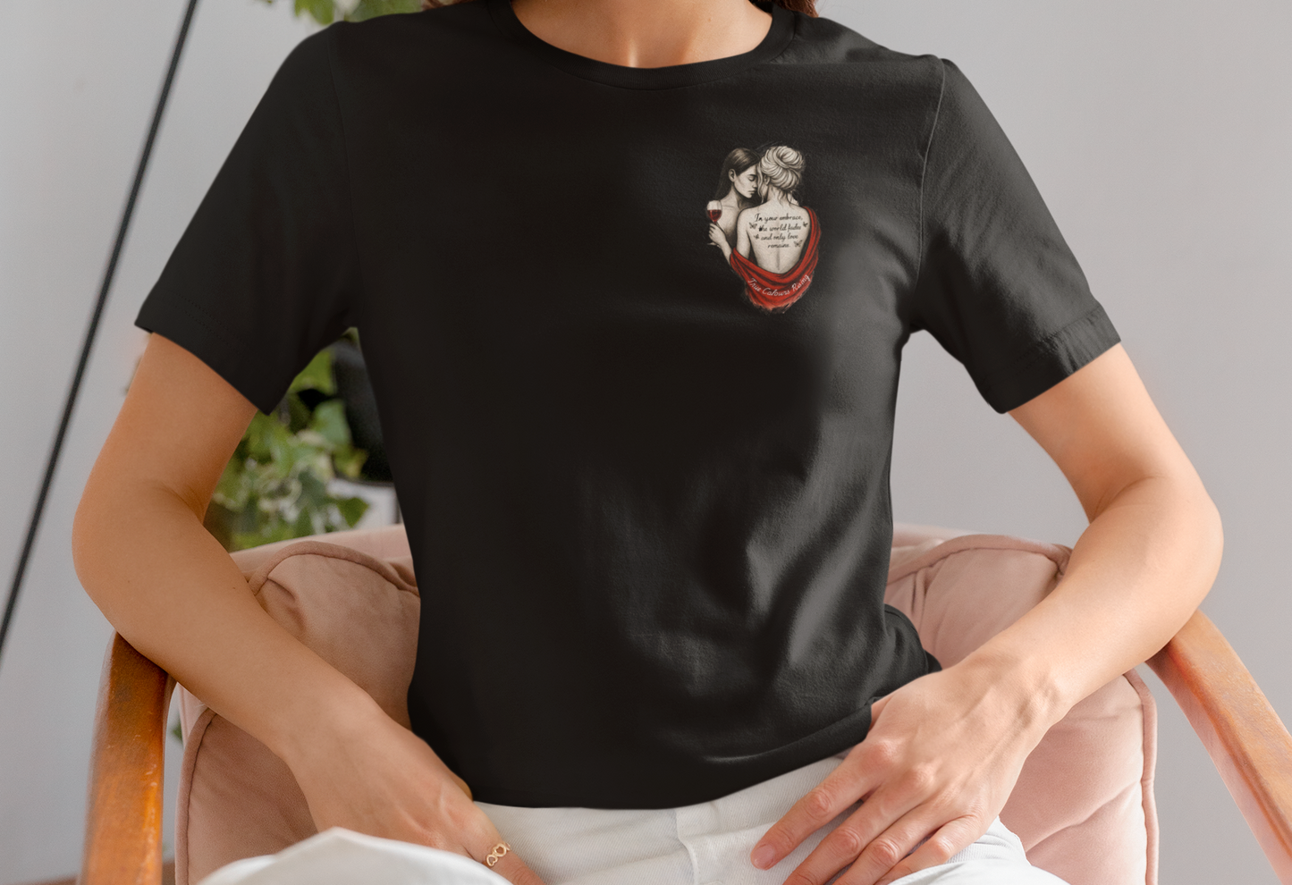 Woman with wavy brown hair wearing a black t-shirt featuring two women holding a wine glass, with text tattooed on one woman's back, reading: "In your embrace, the world fades and nothing else matters