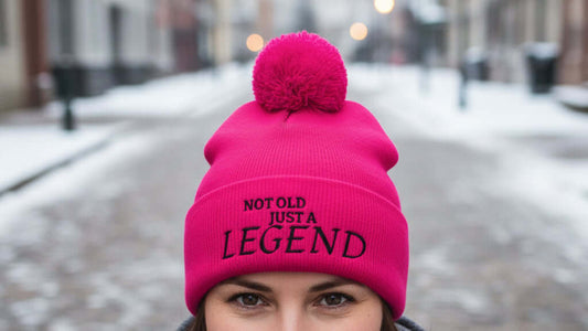 Pink beanie with pom-pom and 'Not Old Just a Legend' text on a white background
