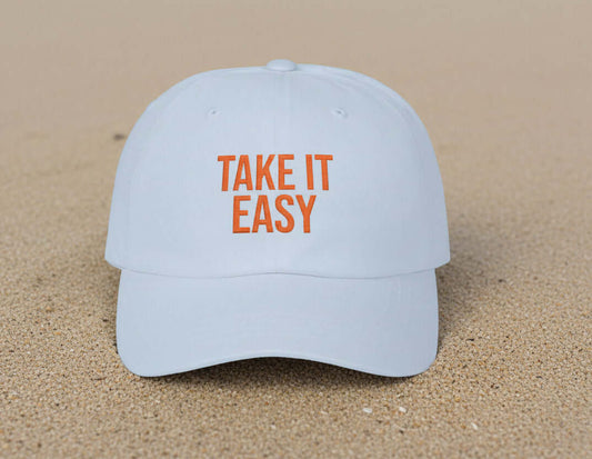 Take It Easy dad cap in natural sand with orange embroidery worn outdoors by the water