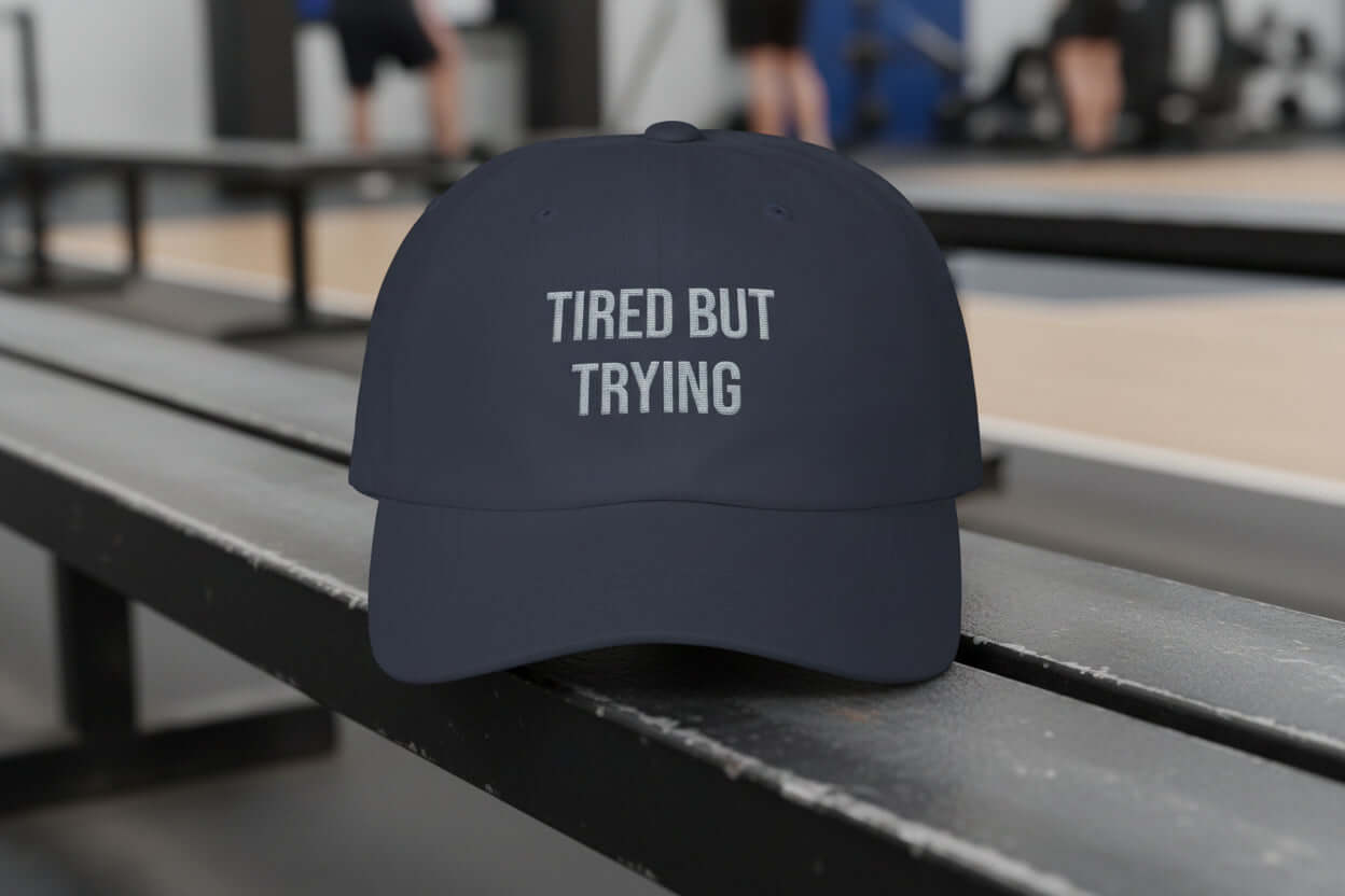 Navy dad cap with white embroidered text reading “Tired But Trying” on the front, unstructured low profile design
