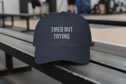 Navy dad cap with white embroidered text reading “Tired But Trying” on the front, unstructured low profile design
