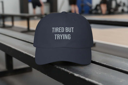 Navy dad cap with white embroidered text reading “Tired But Trying” on the front, unstructured low profile design