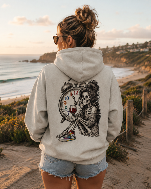 Woman wearing the Queer Vintage Timeless Spirits hoodie with vintage skeleton back print overlooking the coastline at sunset.