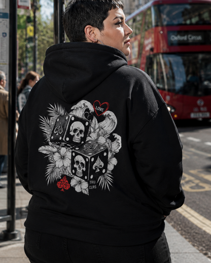 Plus-size woman wearing the Love Is a Gamble black hoodie at a London bus stop on a sunny day.