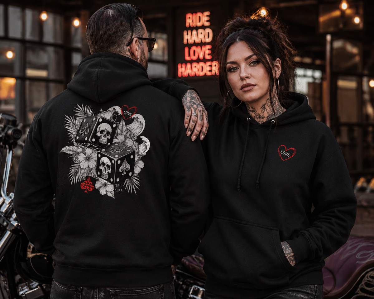 Biker couple wearing Love Is a Gamble hoodies, with the woman's front heart design visible and the man's back displaying the gothic skull dice artwork.