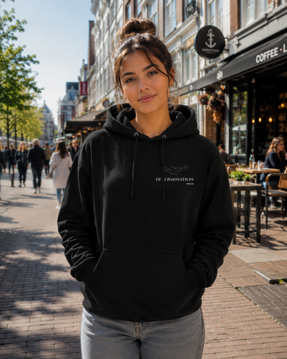 Woman wearing the IMPOSSIBILITY BECOMES POSSIBLE WITH DETERMINATION premium black hoodie featuring the minimalist Determination chest motif in a bright urban setting.