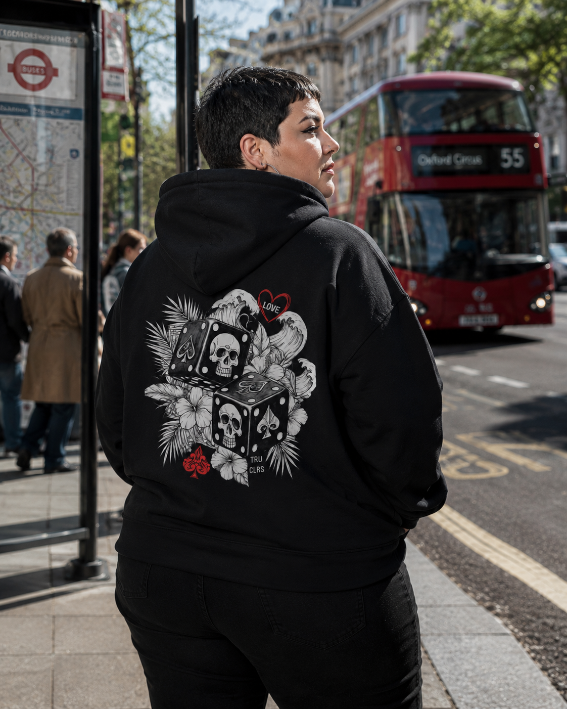 Woman standing with her back to the camera wearing the Love Is a Gamble hoodie showcasing the large skull dice artwork against a London city backdrop.