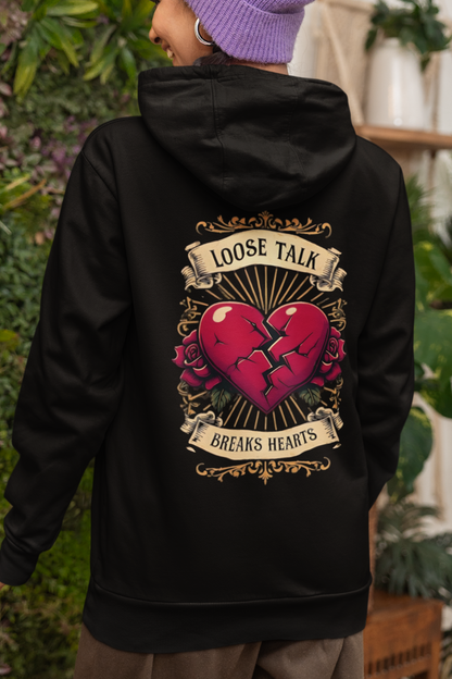 Person wearing a black hoodie with a vintage graphic design on the back, standing in an indoor setting with plants. heart broken but healing