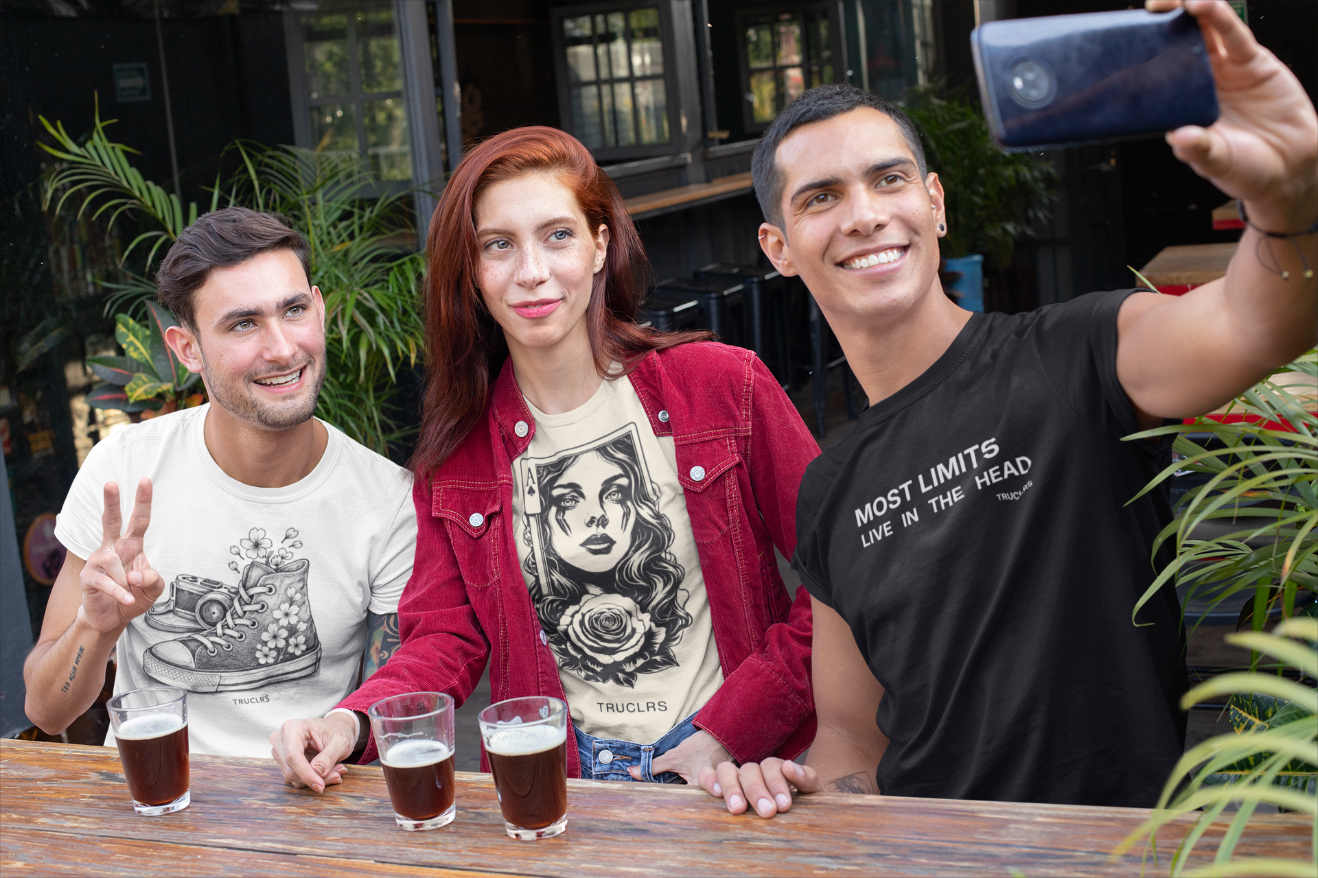 Three friends taking a selfie at an outdoor bar with drinks wearing true colours t shirts